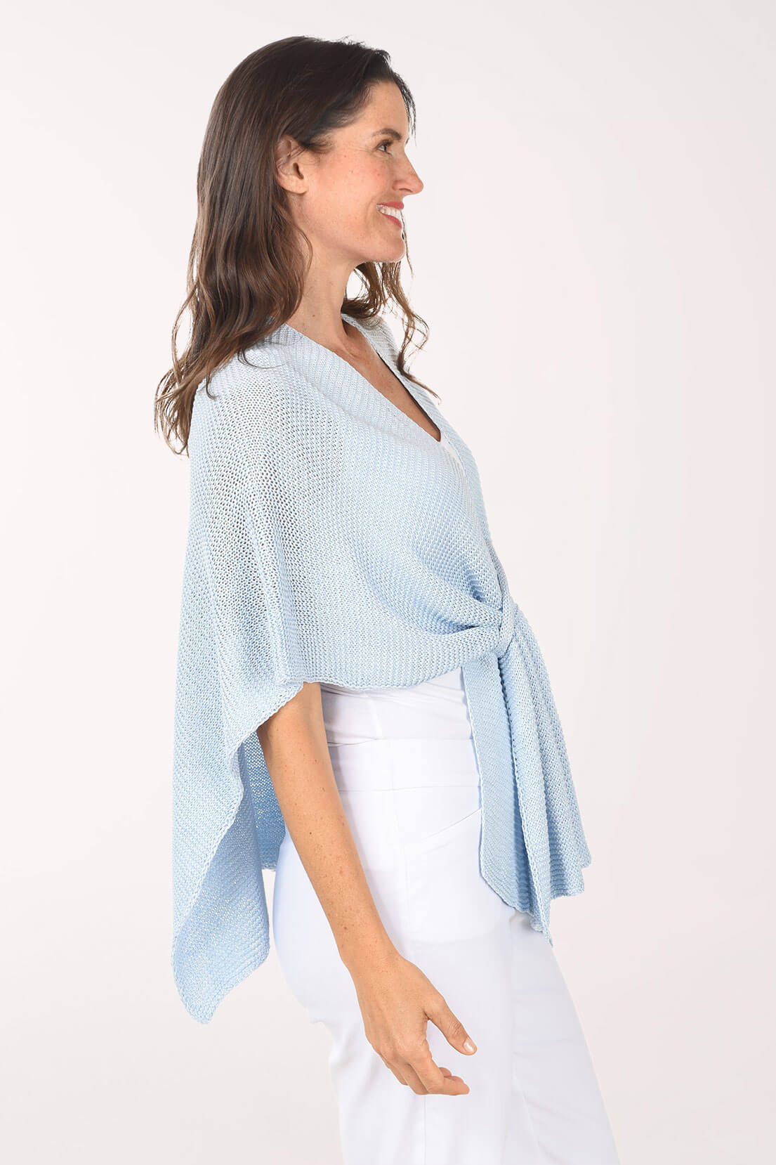 Side shot of a woman wearing a light blue poncho against a white background