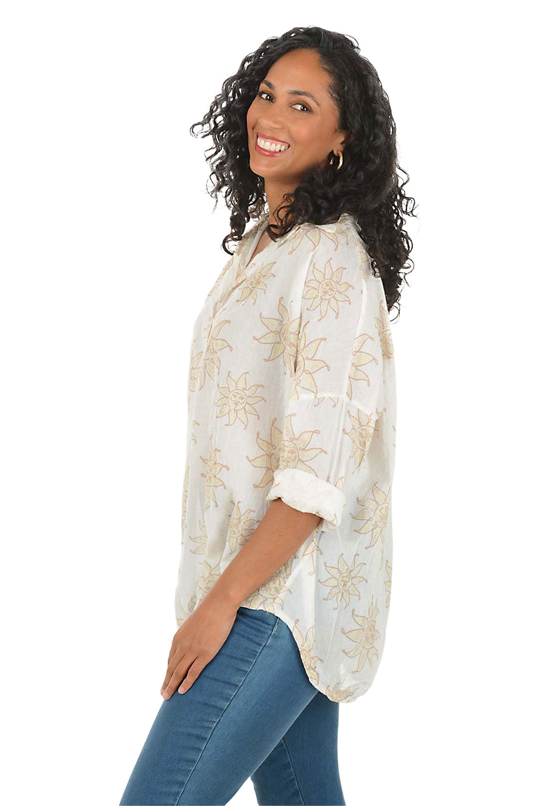 Woman wearing a white blouse with floral patterns and blue jeans on a white background. Side shot.
