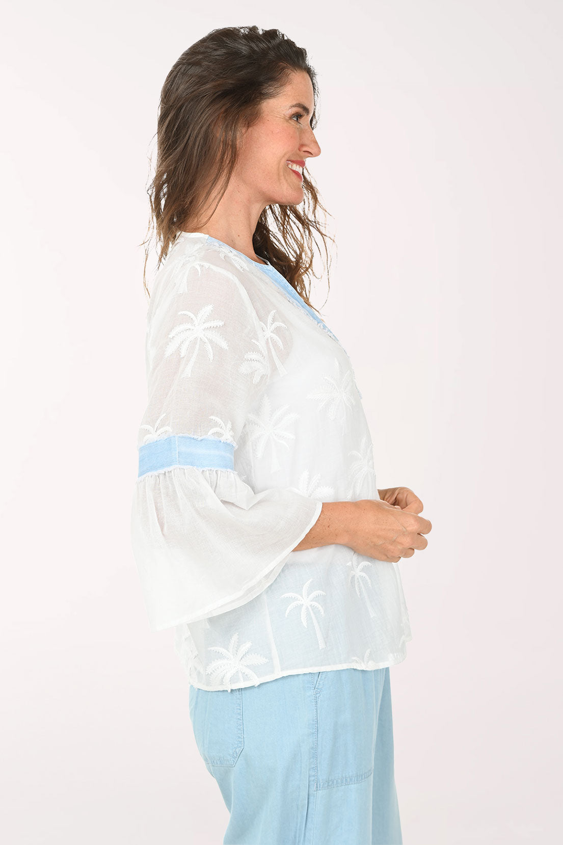Woman wearing a white blouse with blue accents and light blue pants on a white background