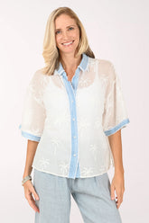 Woman wearing a white embroidered blouse with light blue trim on a white background