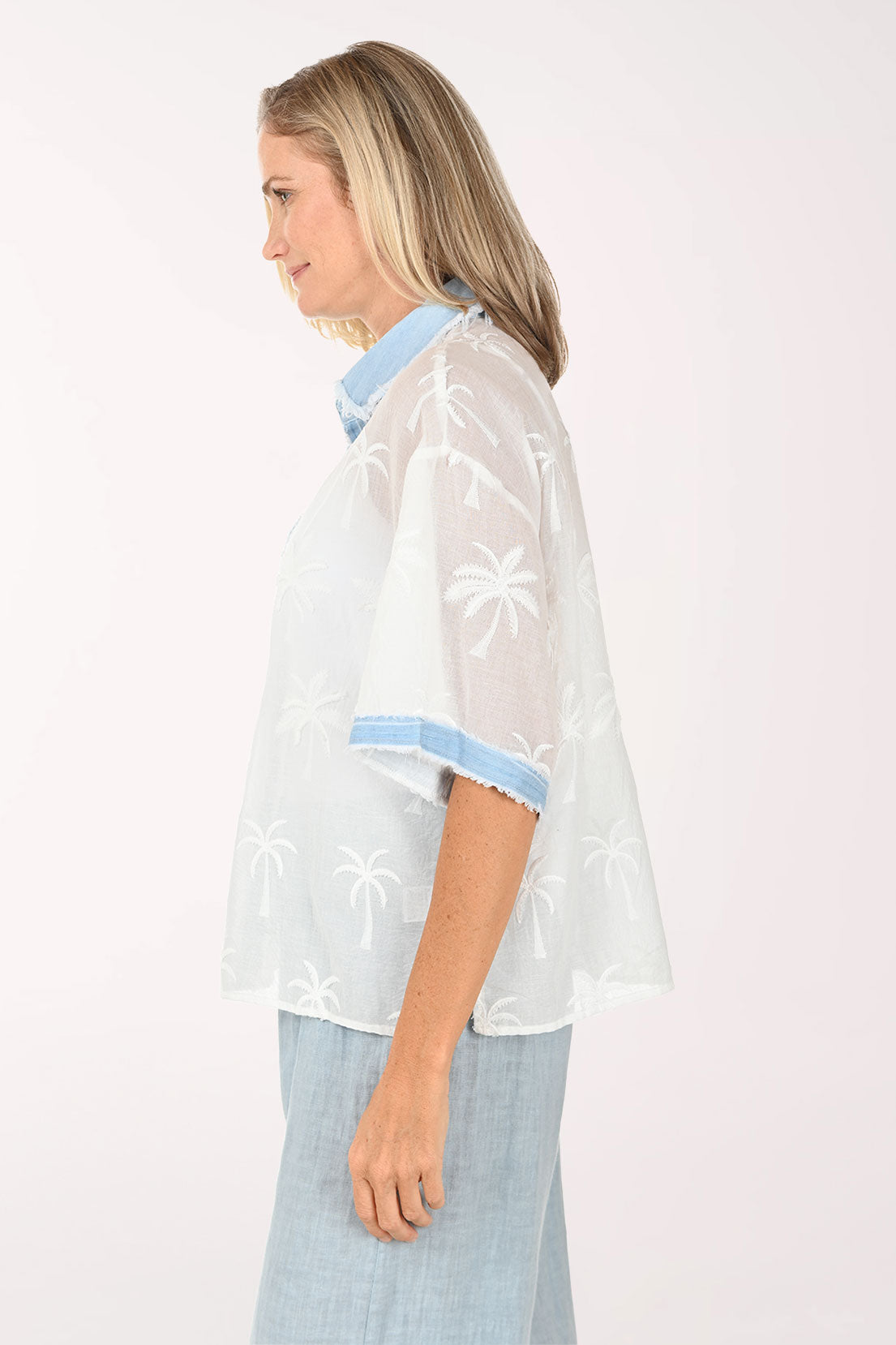 Woman wearing a white embroidered blouse with light blue trim on a white background