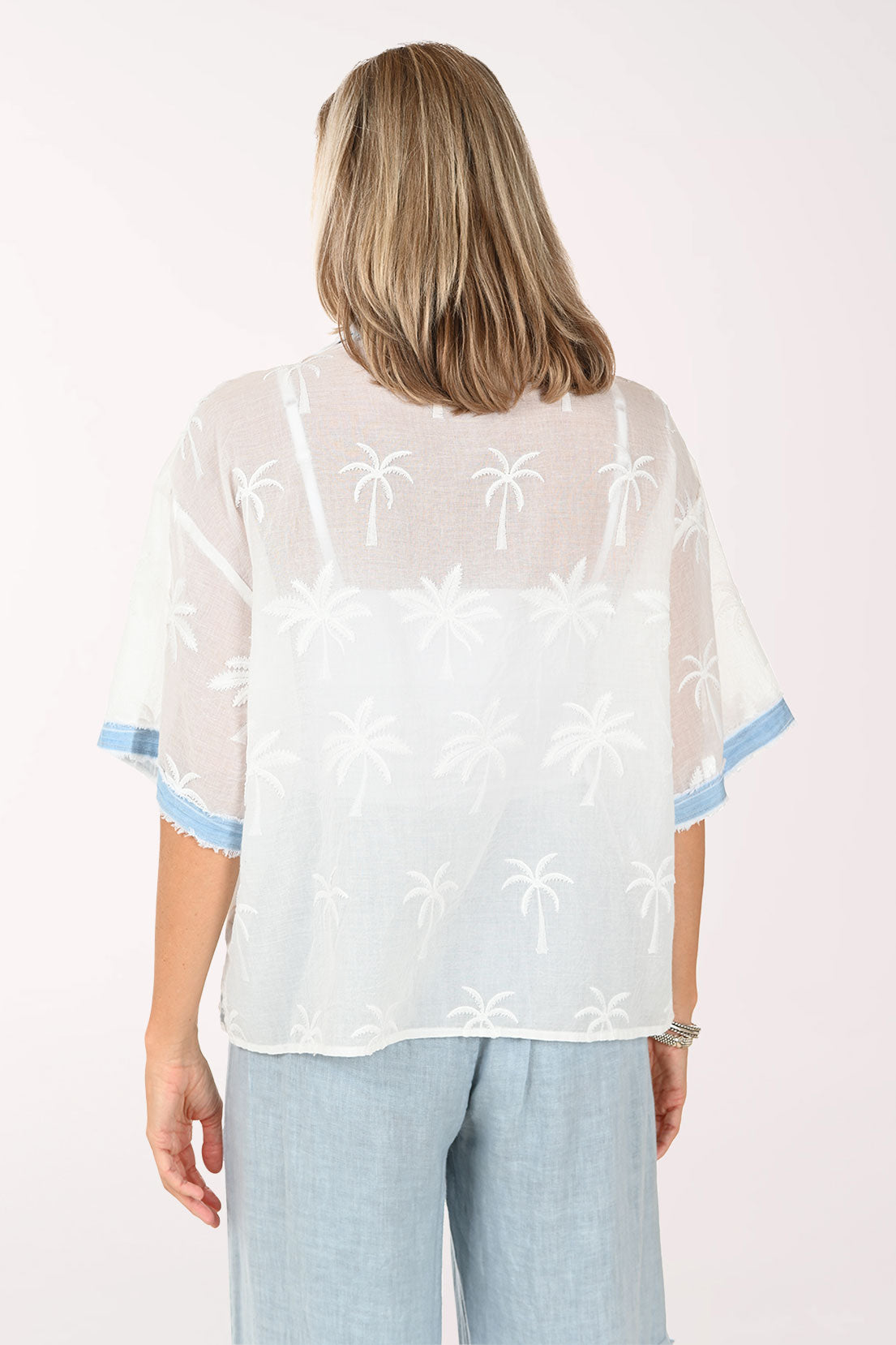 Woman wearing a white embroidered blouse with light blue trim on a white background