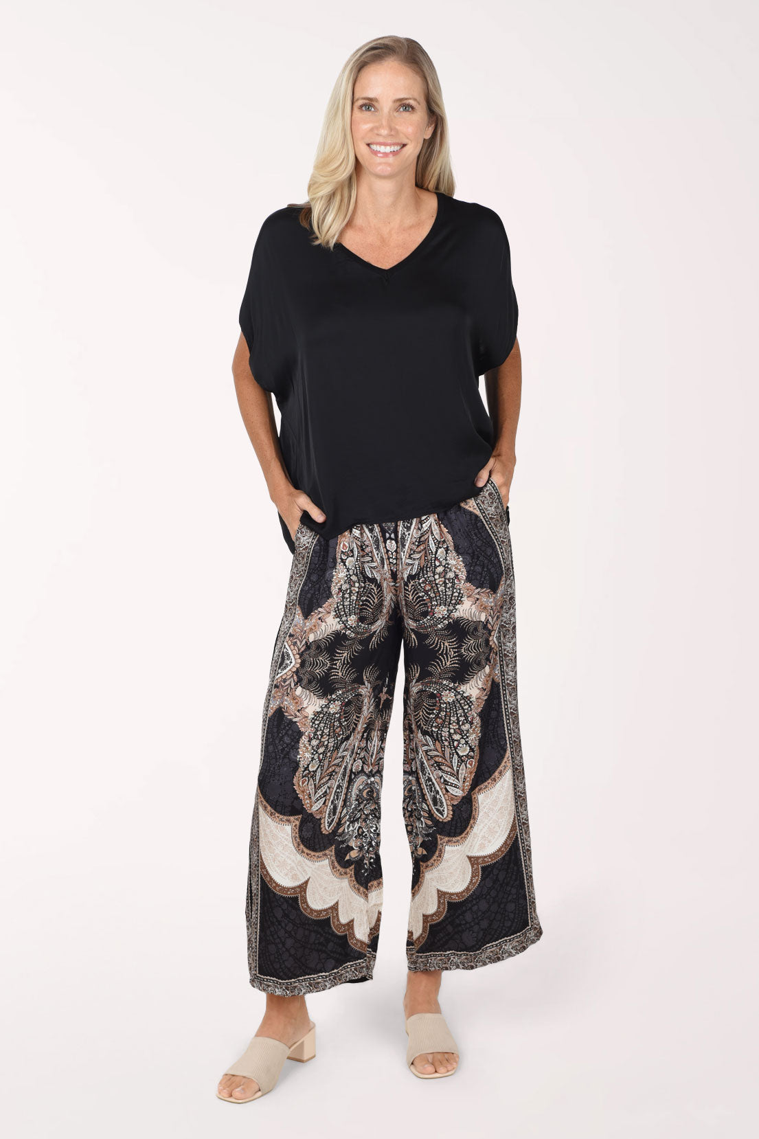 Woman wearing a black silky dolman sleeve top with black paisley flared pants 