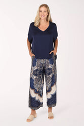 A woman modeling a navy blue short-sleeve V-neck top and matching navy wide-leg pants with a beige and blue paisley pattern, standing against a plain white studio background.