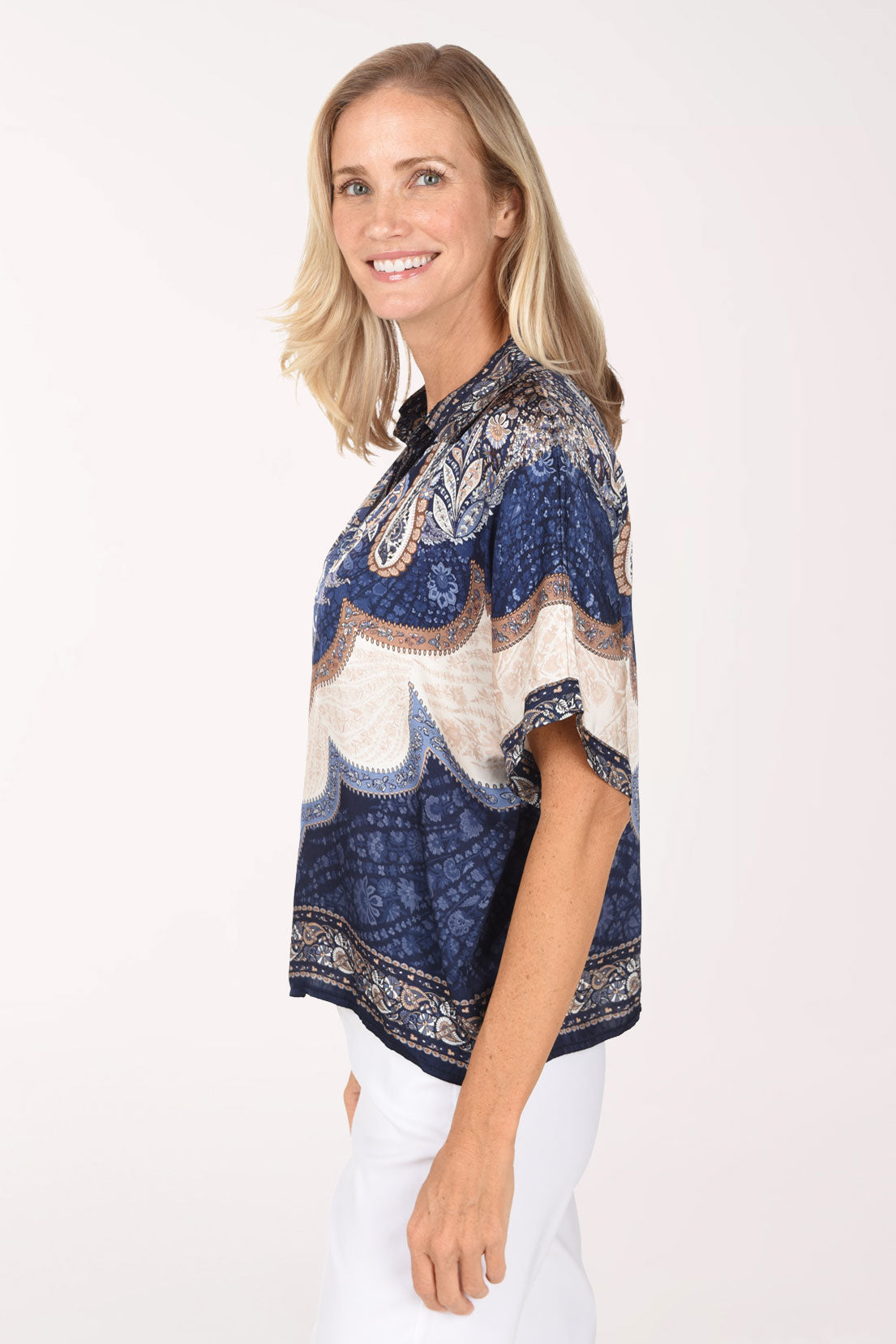 A woman wearing a short-sleeve V-neck blouse with a blue, beige, and white paisley pattern, photographed against a plain light background.