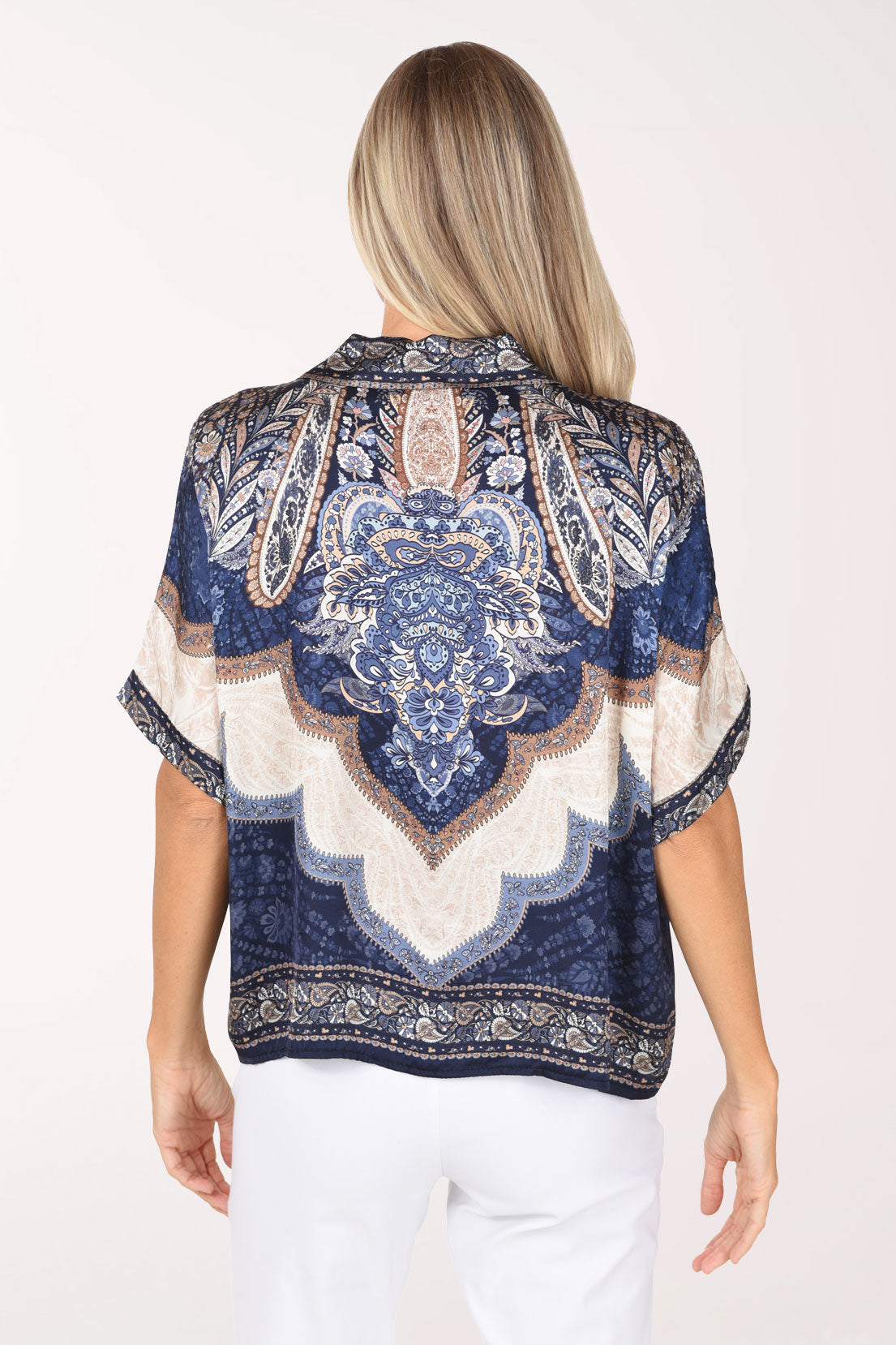 A woman wearing a short-sleeve V-neck blouse with a blue, beige, and white paisley pattern, photographed against a plain light background.