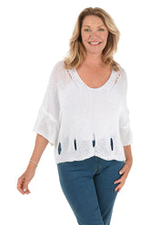 A front shot of a model wearing a white open knit slouchy sweater with a scoop neck and 3/4-length dolman sleeves. The sweater has a shark bite hemline with cut-out details.