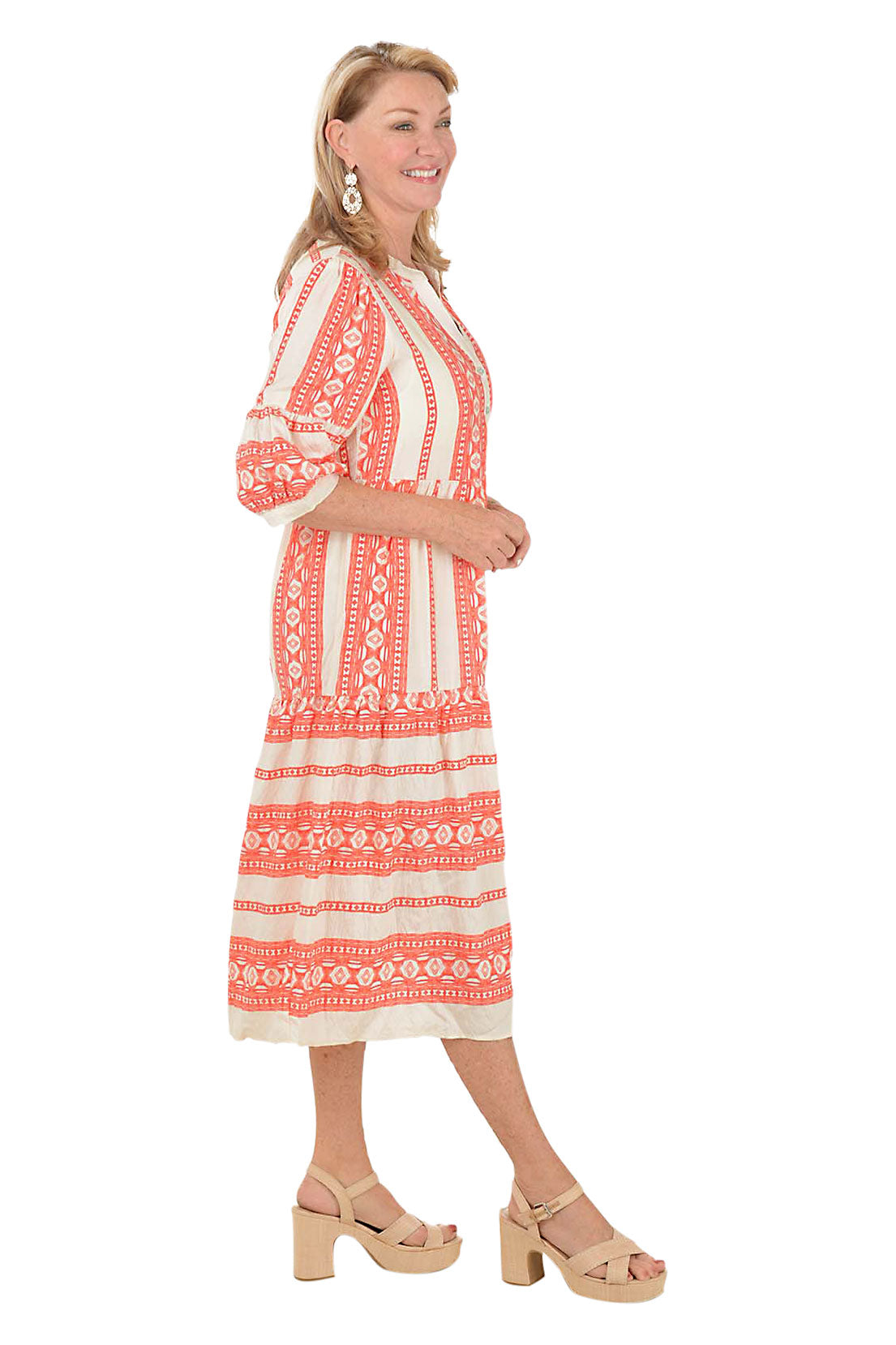 Woman wearing a coral and white patterned midi dress on a white background. Side shot.