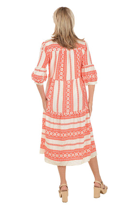 Woman wearing a coral and white patterned midi dress on a white background. Back shot.