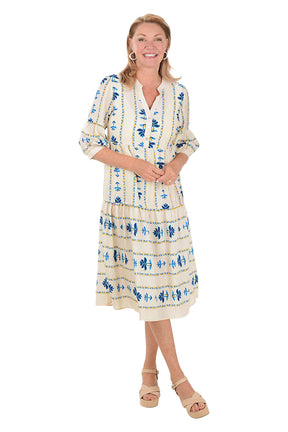 Woman wearing a white midi dress with blue floral patterns on a white background. Second front shot.
