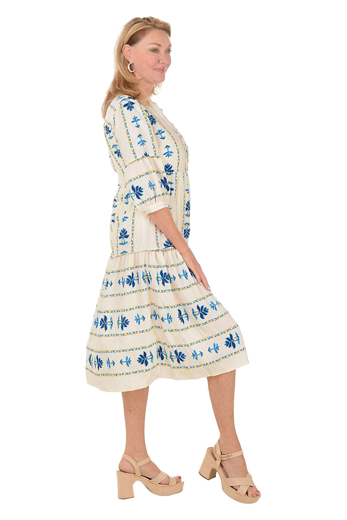 Woman wearing a white midi dress with blue floral patterns on a white background. Side shot.