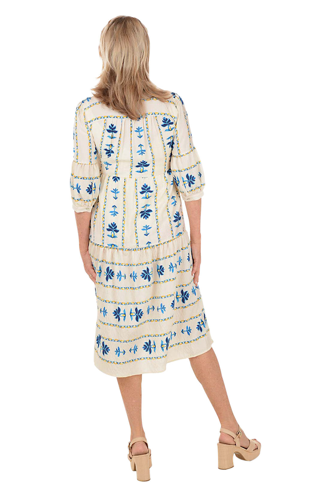 Woman wearing a white midi dress with blue floral patterns on a white background. Back shot.