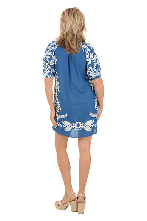 Woman wearing a blue dress with white floral patterns on a white background. Back shot.