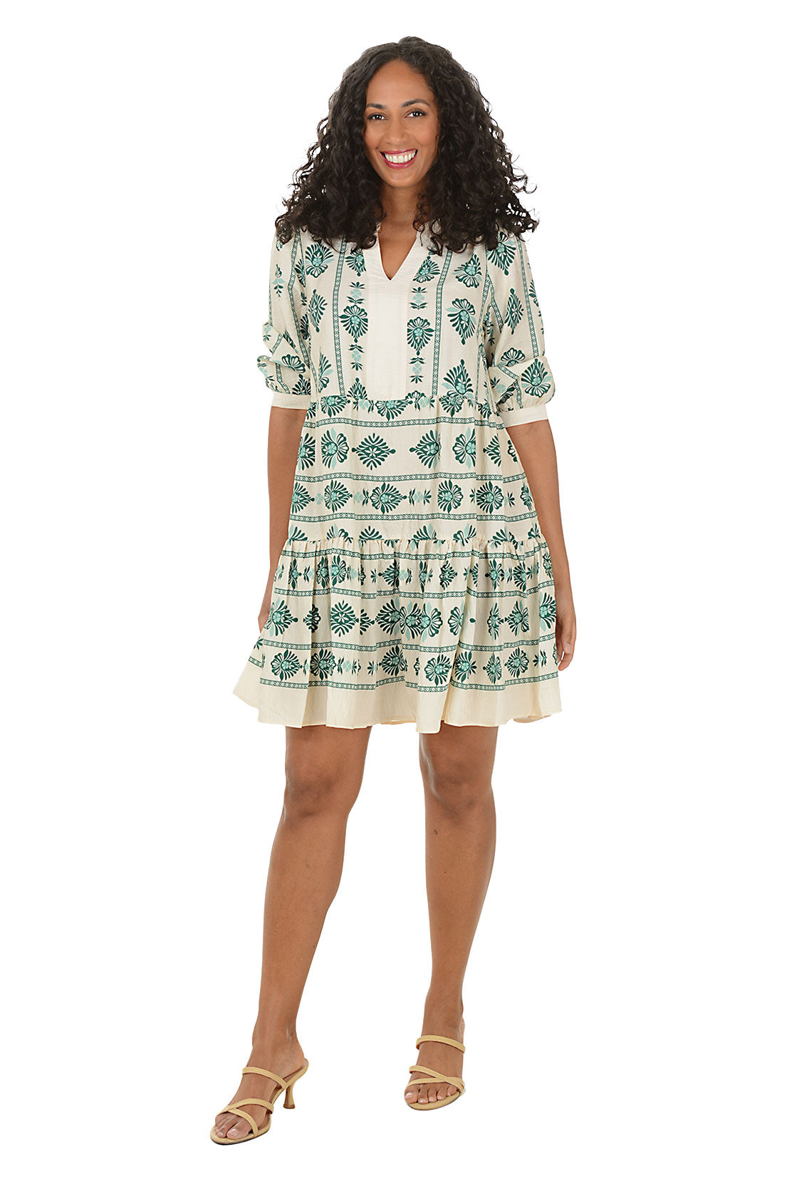 Woman wearing a 3/4 sleeve green and white patterned dress on a white background.