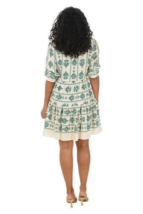Woman wearing a 3/4 sleeve green and white patterned dress on a white background. Back shot.