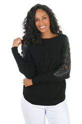 Woman wearing a long sleeve black sweater with scalloped mesh embellishments and rhinestone accents on shoulders.