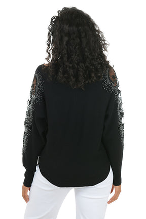 Woman wearing a long sleeve black sweater with scalloped mesh embellishments and rhinestone accents on shoulders. Back shot.