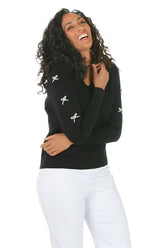 Woman wearing a black sweater with white bow embellishments on the sleeves on a white background.