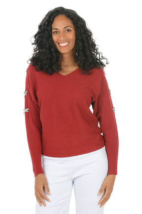 Woman wearing a red sweater with rhinestone bow embellishments on the sleeves on a white background.
