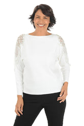 Woman wearing a white long sleeve sweater with sheer mesh angel wing embellishments with beaded and rhinestone accents on shoulders.