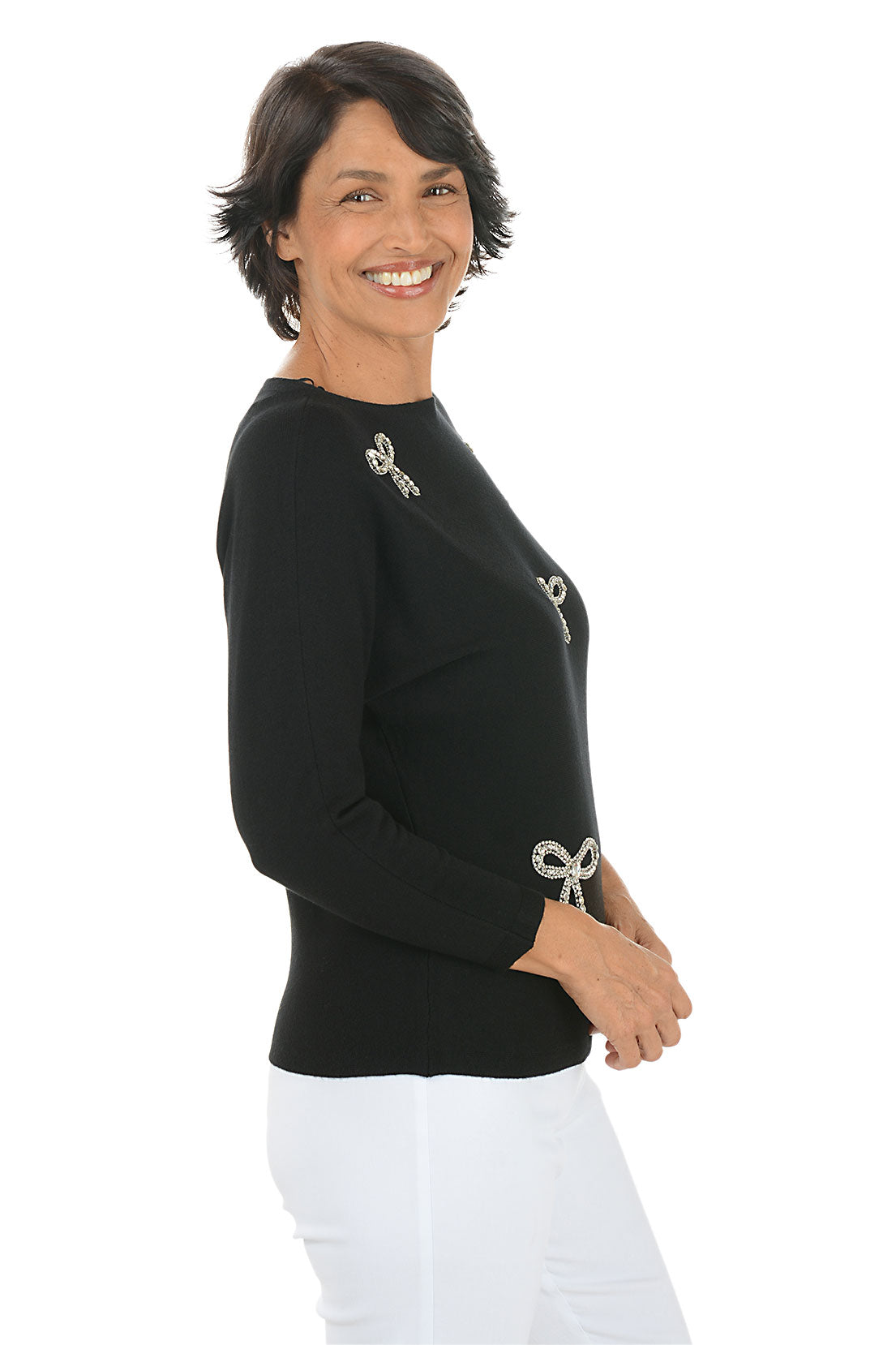 Woman wearing a black long sleeve sweater with rhinestone bow embellishments.  Side shot.