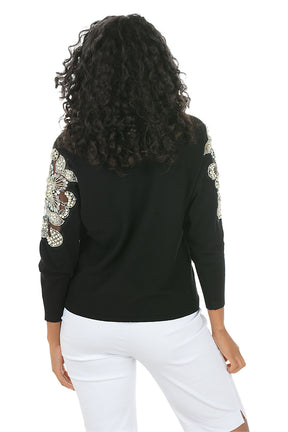 Woman wearing a long sleeve black sweater with floral embellished appliques on the arm. Back shot.