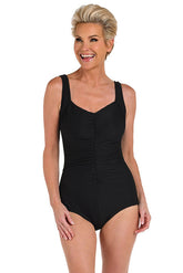 A front shot of a model wearing a solid-colored black one-piece swimsuit with a shirred front and girl leg styling.