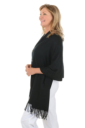 Woman wearing a black shawl with fringes on a white background. Side shot.
