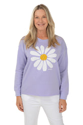 Woman wearing a purple sweater with a white daisy design on a white background.