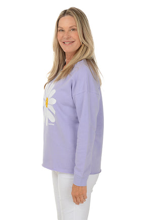 Woman wearing a purple sweater with a white daisy design on a white background. Side shot.