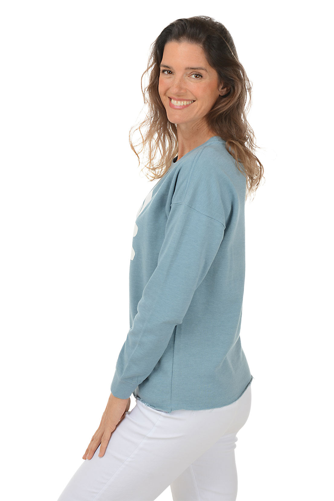 Woman wearing a blue sweatshirt with a white daisy design on a white background. Side shot.