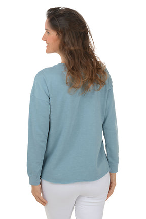 Woman wearing a blue sweatshirt with a white daisy design on a white background. Back shot.