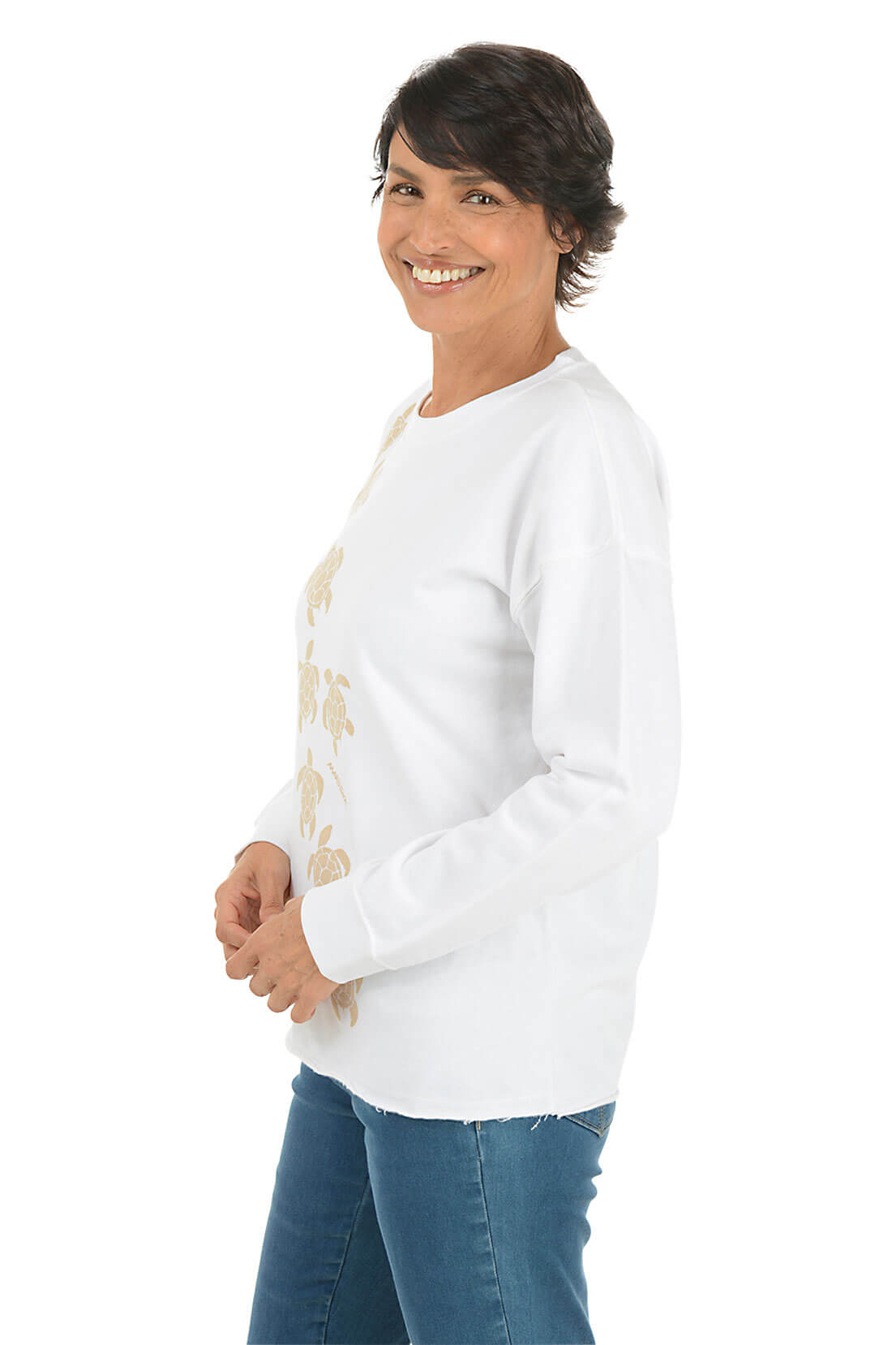 Woman wearing a white long-sleeve shirt with turtle designs on a white background. Side shot.