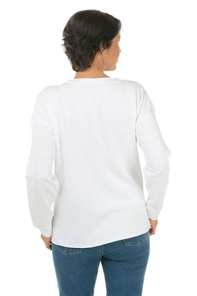 Woman wearing a white long-sleeve shirt with turtle designs on a white background. Back shot.