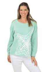 Woman wearing a light green sweater with a white starfish design on a white background.