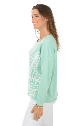 Woman wearing a light green sweater with a white starfish design on a white background. Side shot.