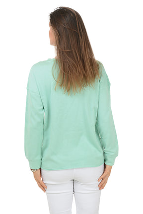 Woman wearing a light green sweater with a white starfish design on a white background. Back shot.