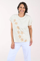 Woman wearing a beige t-shirt with turtle patterns on a plain background
