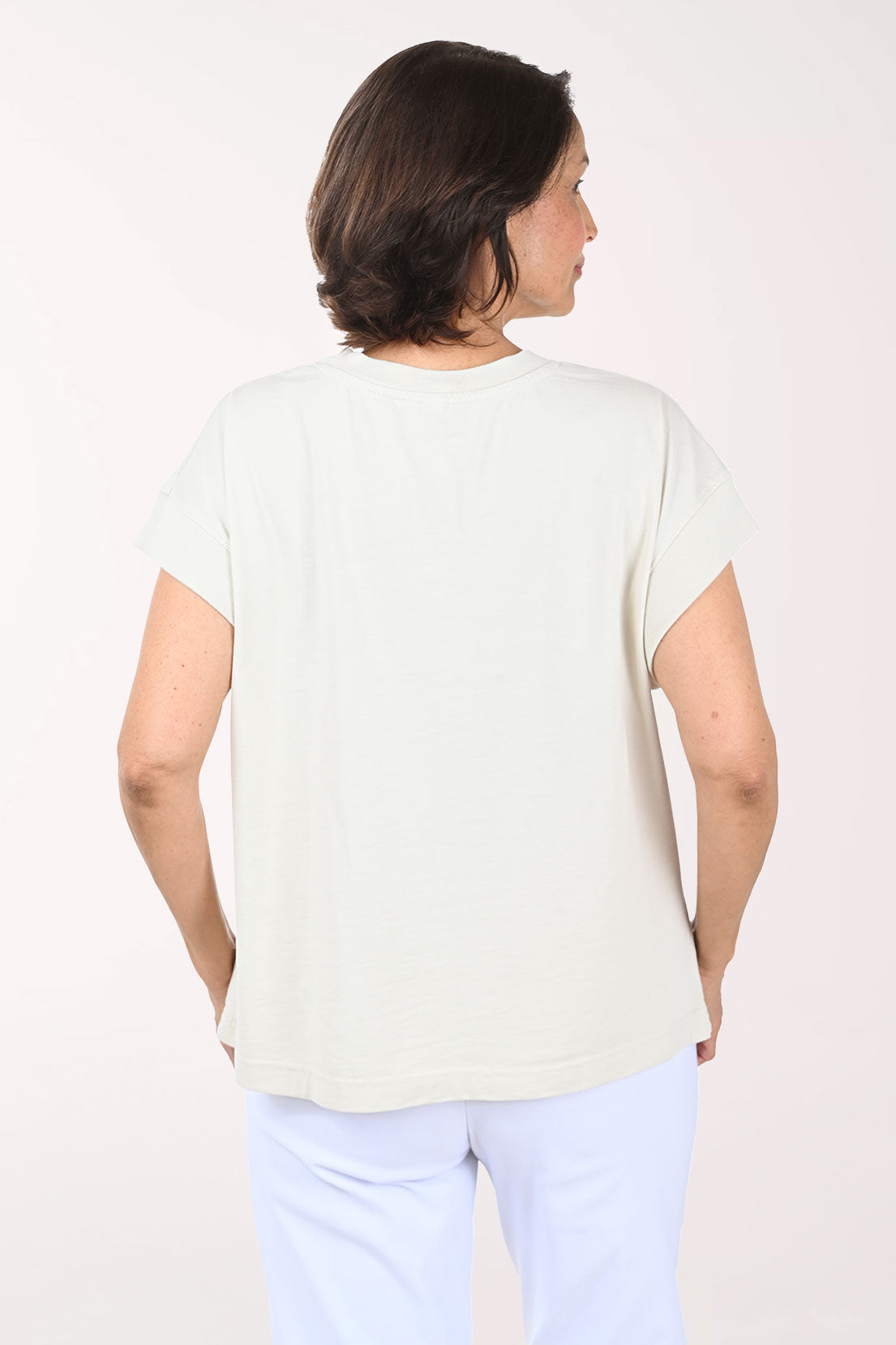 Woman wearing a beige t-shirt with turtle patterns on a plain background