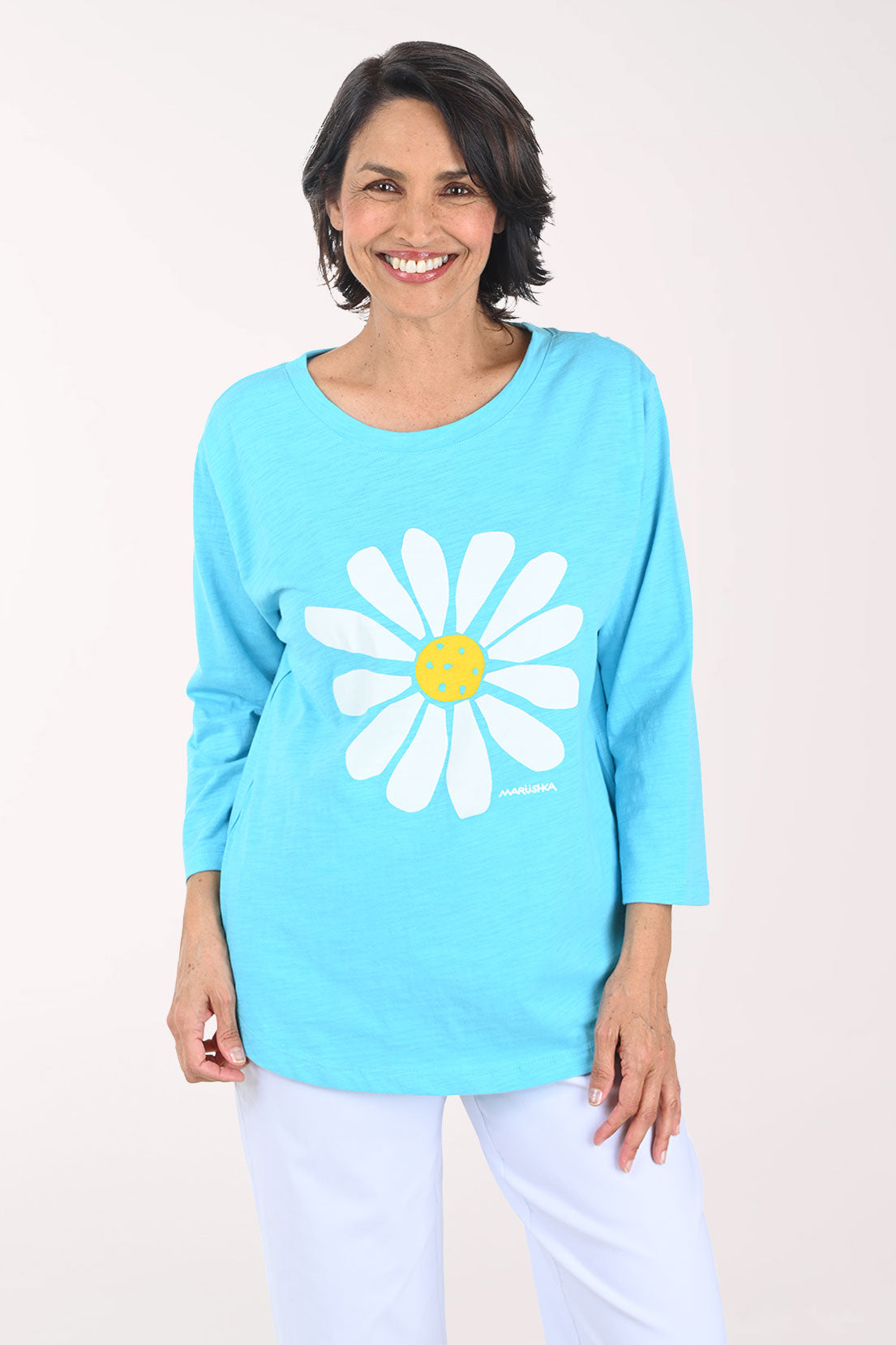 Woman wearing a light blue tunic top with a white daisy design on a plain background