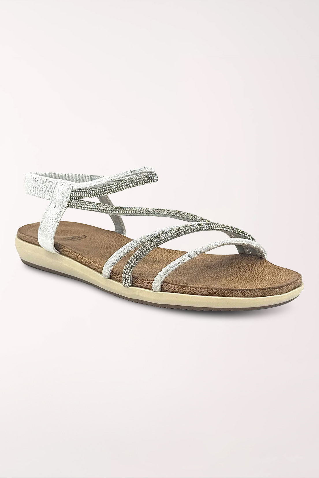 Silver flat sandal with slim crisscrossing rhinestone straps, an elastic rhinestone slingback, tan cushioned footbed and cream sole, shown at an angle.