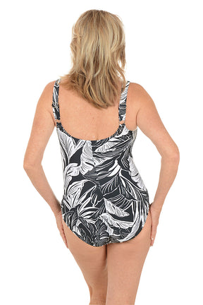 A woman wearing a one piece black and white tropical print swimsuit. Back shot.