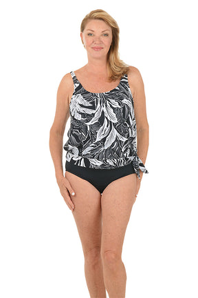 Woman wearing a black and white patterned tankini top with black bottoms on a white background. Full length shot.