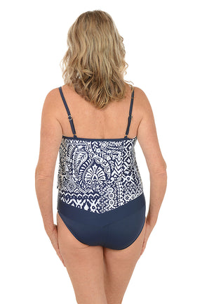 A woman wearing a blue and white one piece swimsuit with a flutter hem. Back shot.