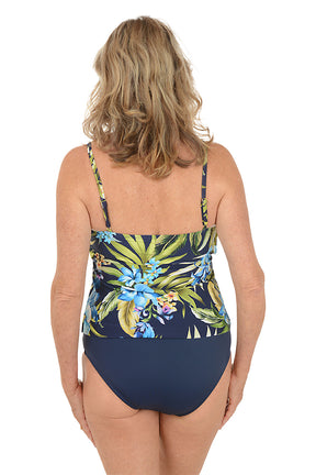 A woman wearing a double tiered navy blue tankini top with a blue and green floral pattern. Back shot.