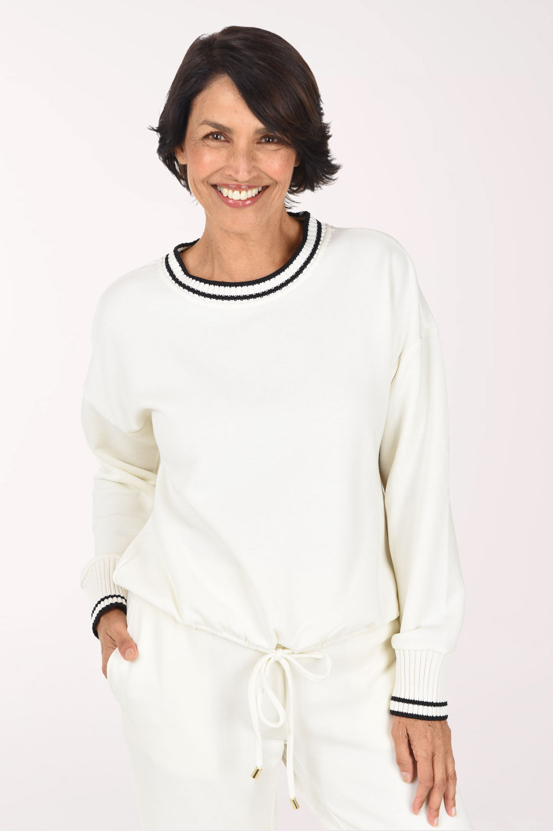 A smiling woman with short dark hair wearing a cream-colored knit sweater and matching sweatpants with black and white striped ribbed trim.