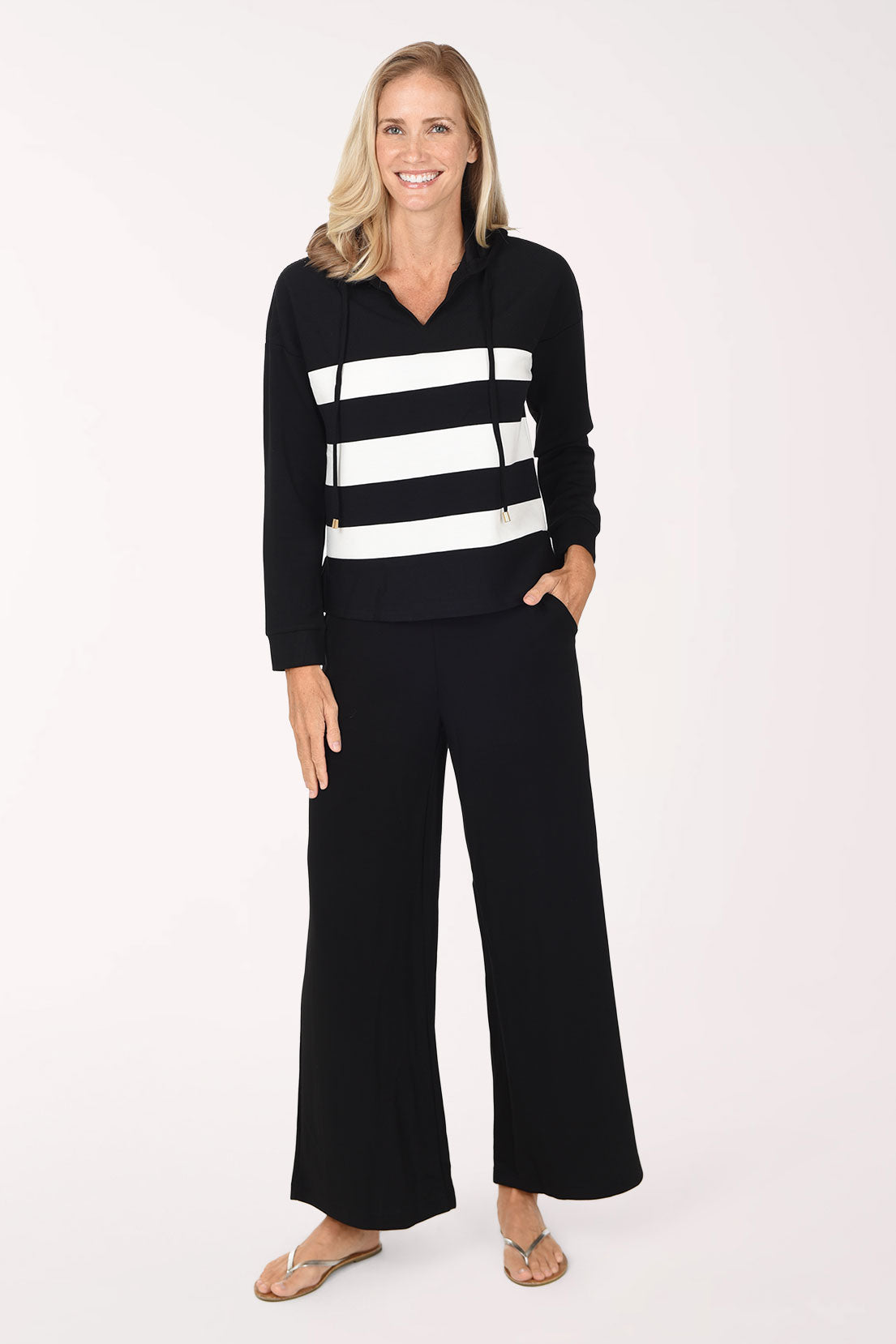 A woman wearing a black/white striped long-sleeve hooded top and matching black pants, standing against a plain white studio background.