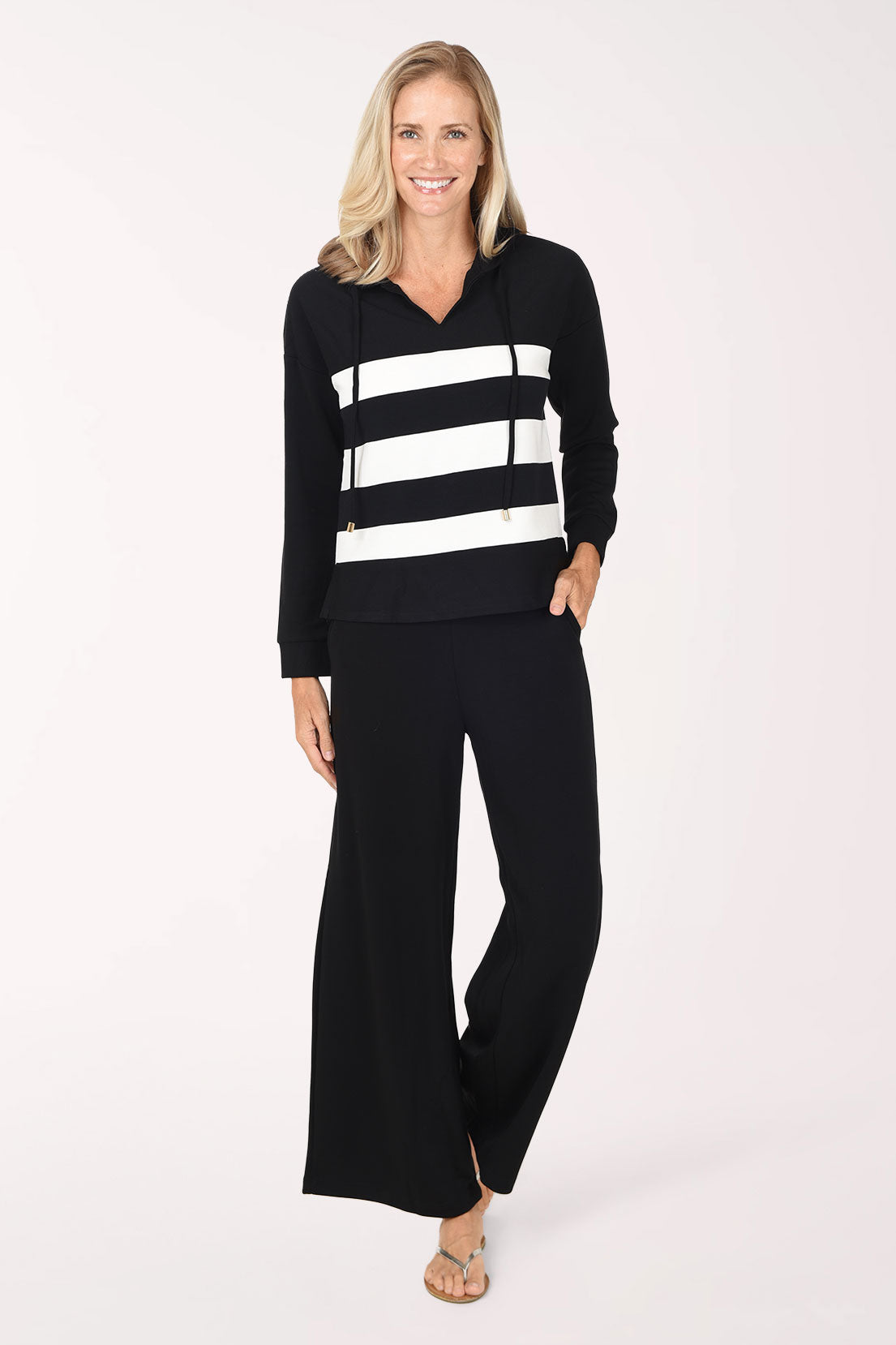 A woman wearing a black/white striped long-sleeve hooded top and matching black pants, standing against a plain white studio background.
