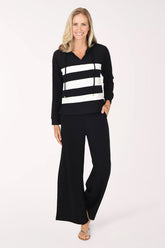 A woman wearing a black/white striped long-sleeve hooded top and matching black pants, standing against a plain white studio background.