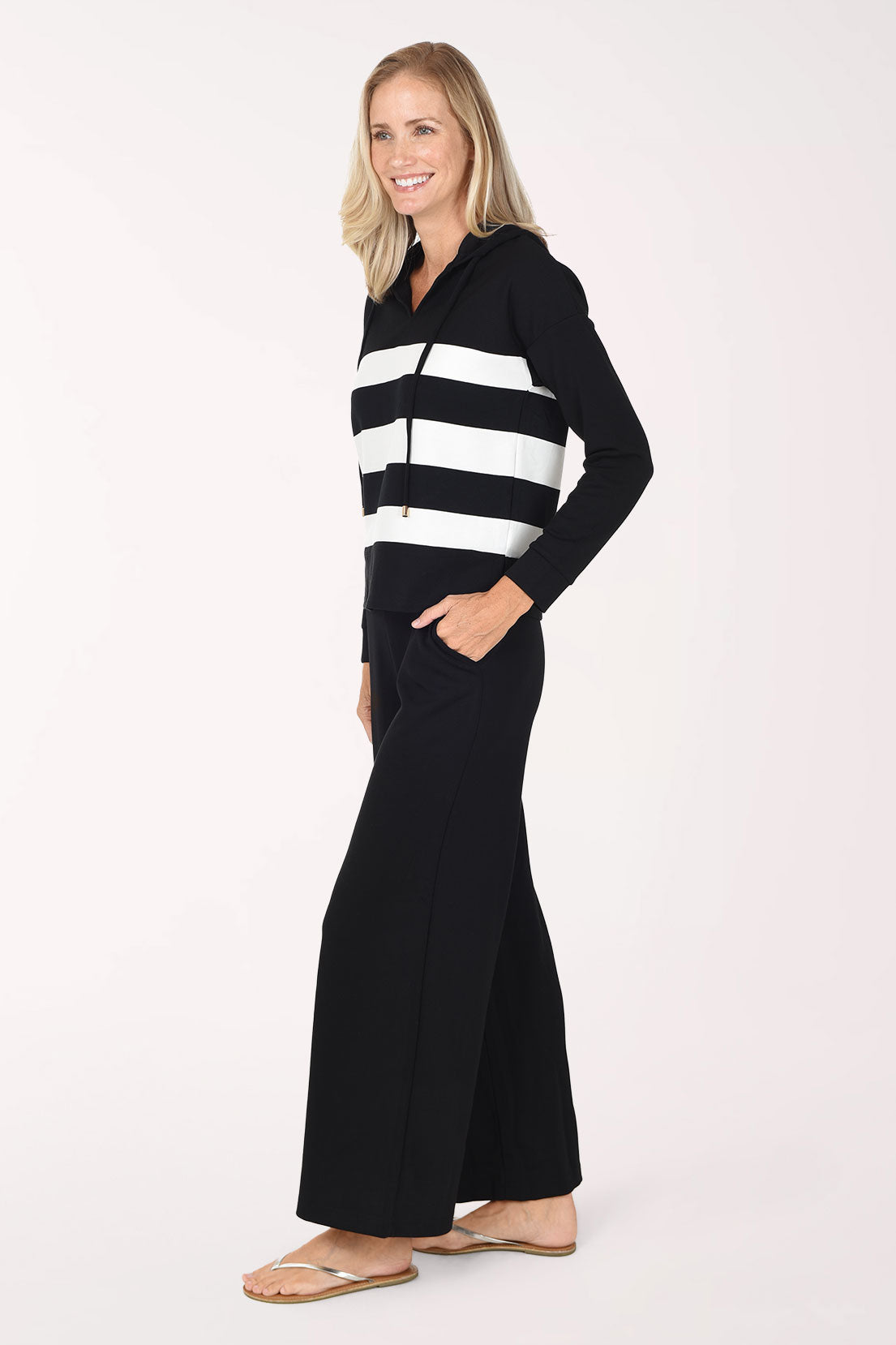 A woman wearing a black/white striped long-sleeve hooded top and matching black pants, standing against a plain white studio background.